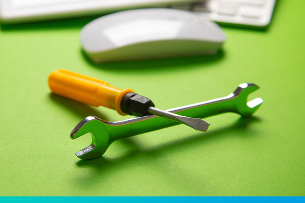 Schraubendreher liegt auf Schraubenschlüssel vor einer Computermaus und -tastatur