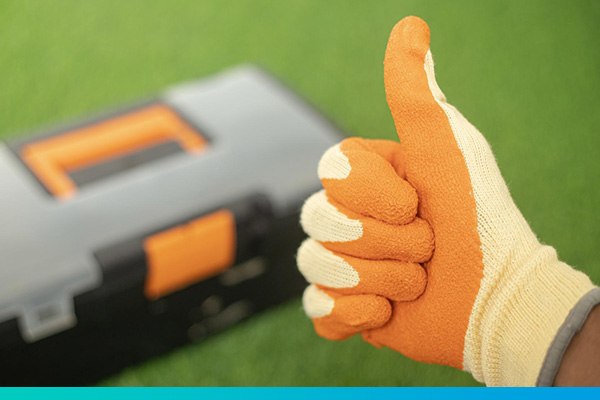 Hand in Arbeitshandschuh hält den Daumen hoch, im Hintergrund ist unscharf ein Werkzeugkoffer zu sehen