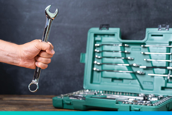 Eine Hand hält einen Schraubenschlüssel vor einem Werkzeugkoffer