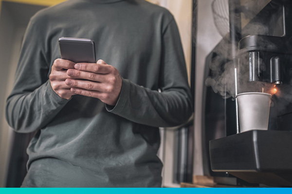Oberkörper eines Mannes mit Telefon vor einer dampfenden Kaffeemaschine