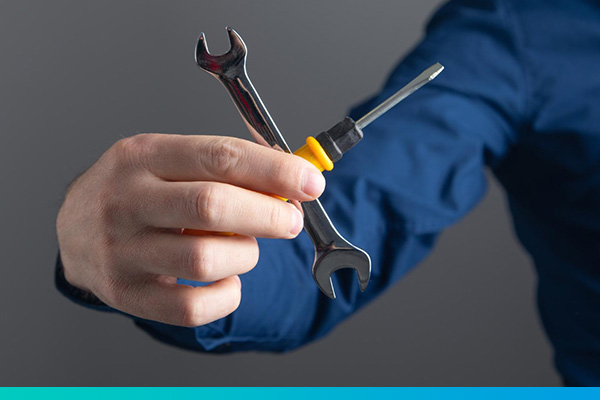 Eine Hand hält einen Schraubenschlüssel und Schraubendreher über Kreuz