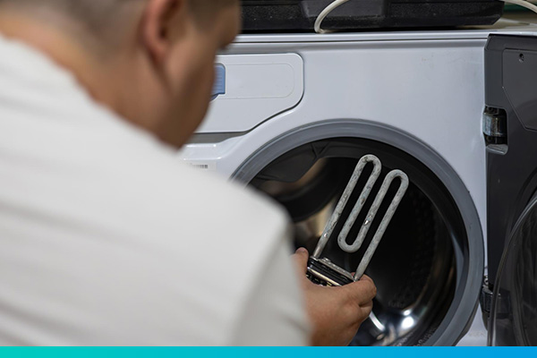 Techniker hält defektes Waschmaschinenteil vor eine geöffnete Waschmaschine