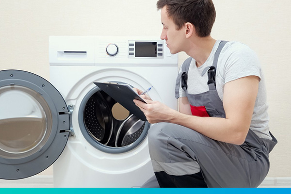 Techniker hockt mit einem Klemmbrett vor einer Waschmaschine
