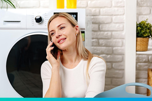 Frau sitzt vor einem Trockner und telefoniert